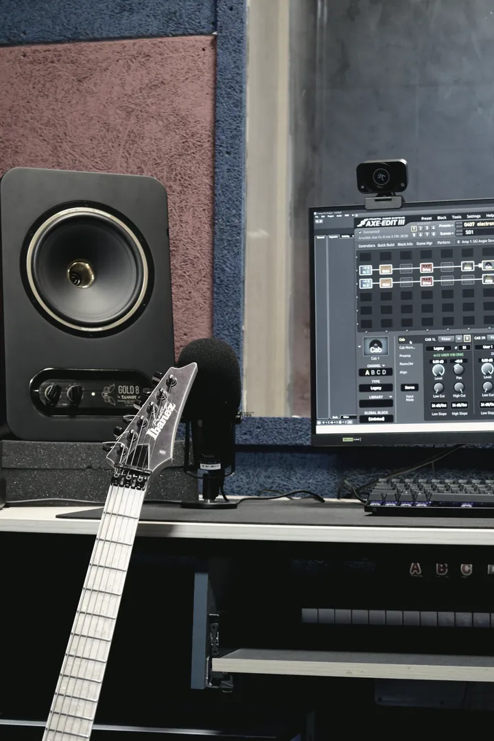 The mix position: a guitar neck resting across the desk, rack processor and nearfield monitor beside the screen.