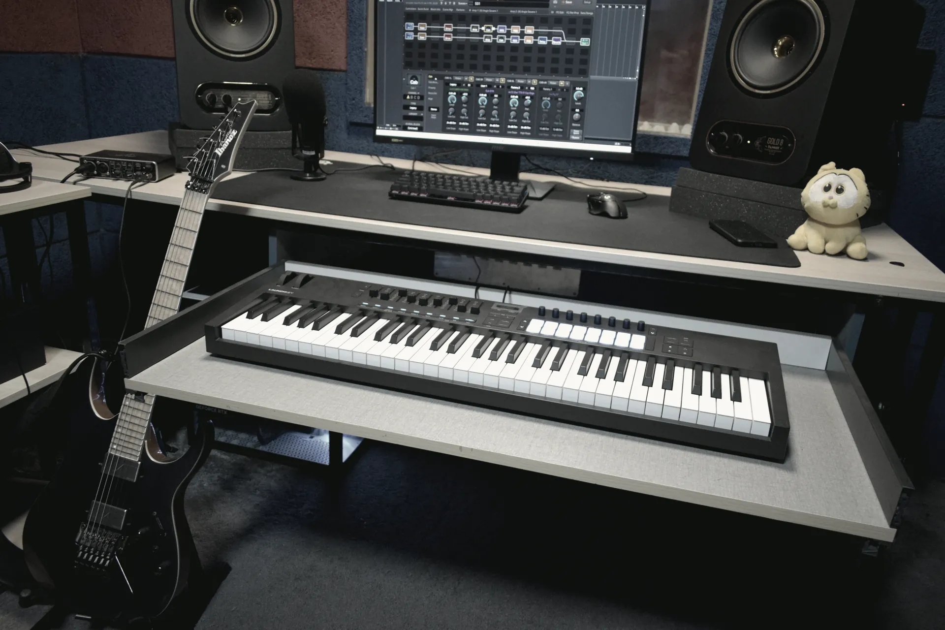 The full desk seen head on: keyboard controller, session screen, monitors either side and the treated wall behind.