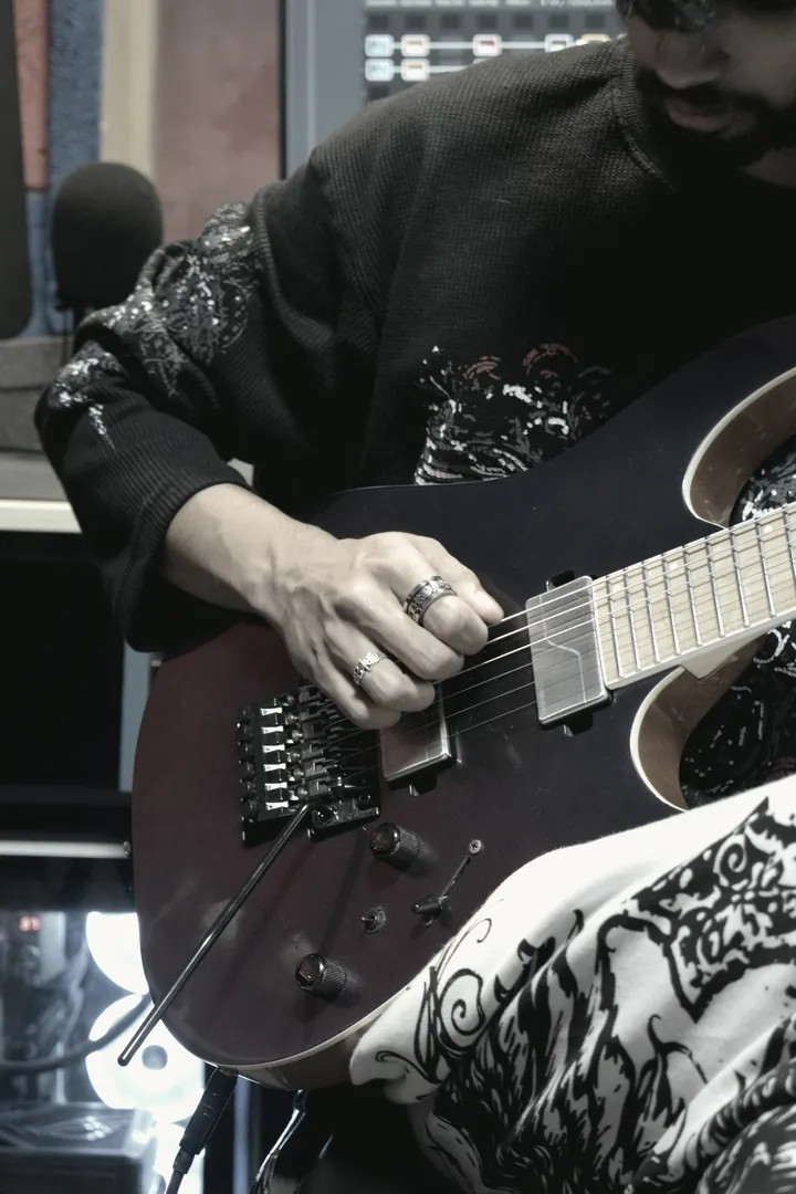 Close frame of a guitar body and a player's patterned sleeve, shot in the live room for campaign use.