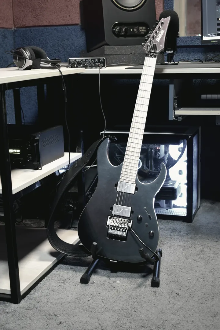 An electric guitar on its stand under the desk shelf, machine lights glowing behind it.