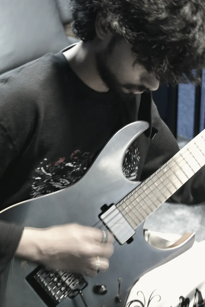 A player's hands working a chord high on the fretboard, lit from the ceiling of the live room.