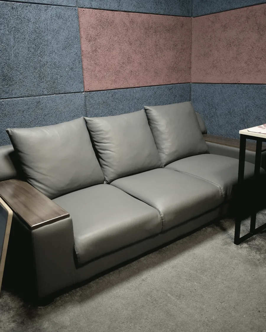 A grey leather couch against the treated wall of the live room, used for listening back.