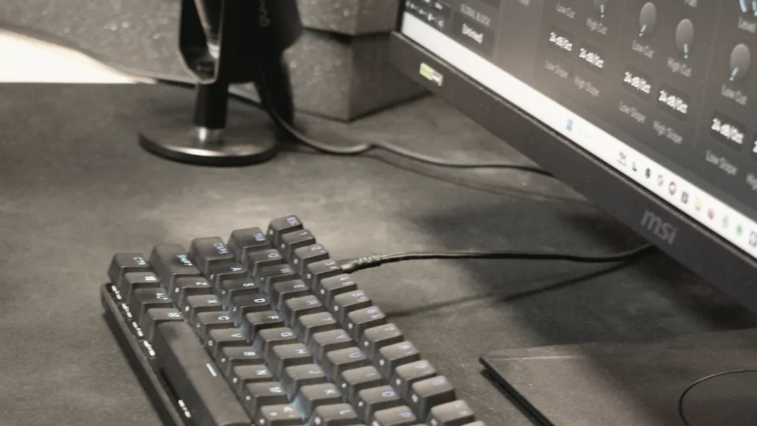 Microphone on a desk stand next to a backlit mechanical keyboard and the session screen.