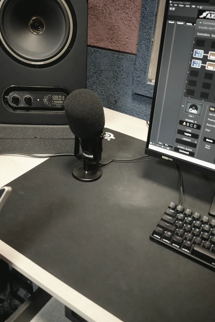 A large-diaphragm microphone on a desk stand beside the screen running the guitar processor editor.
