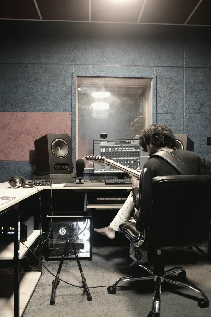 An engineer at the desk mid-session, mic stand in the foreground and the isolation window beyond.