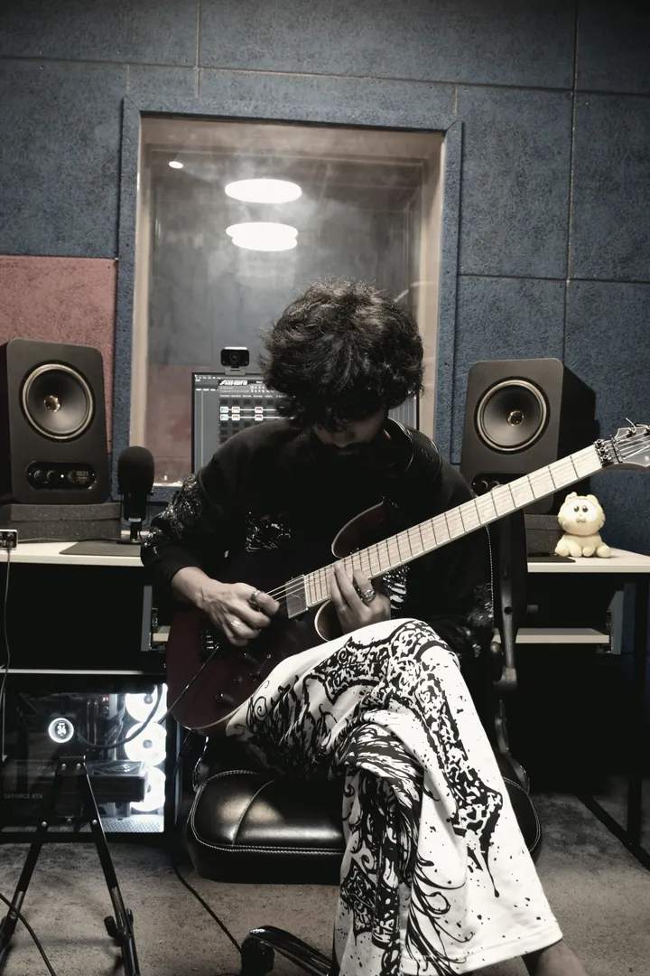 A guitarist seated in the Jayde live room, playing through to the control desk while the isolation window reflects the ceiling light.