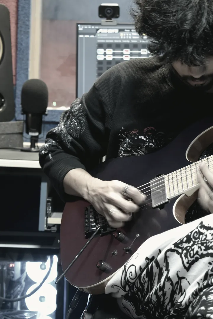 Detail of a hand across the strings above the pickups of an electric guitar.